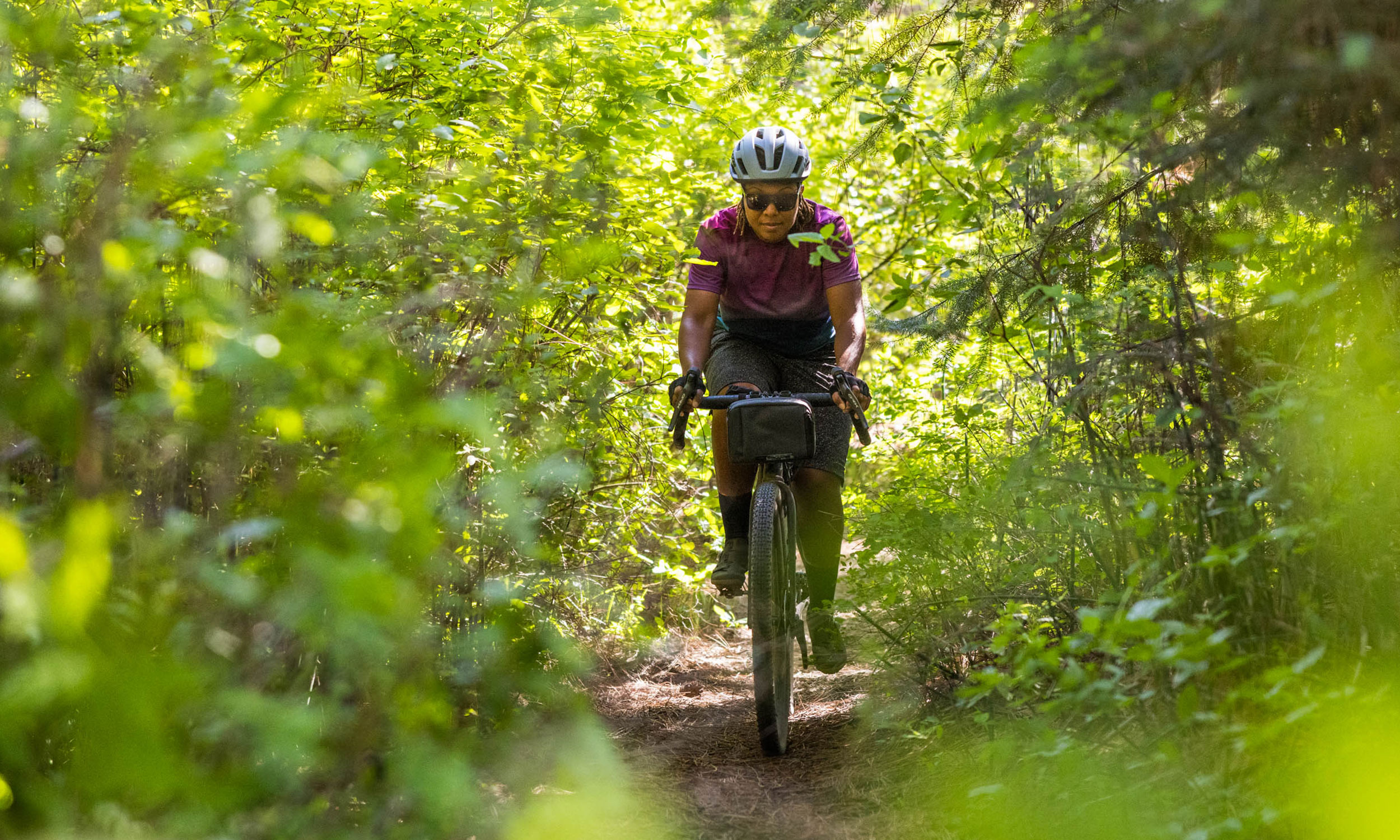 Women riding her shimano GRX 12-speed gravel bike on a single track through the trees