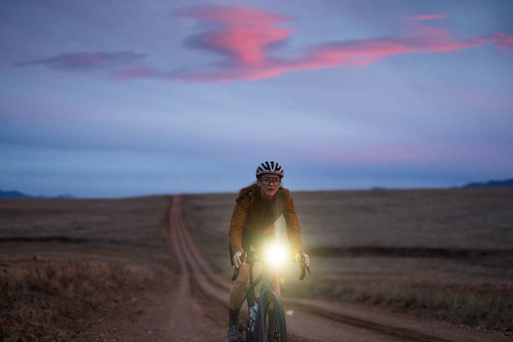 Mulher pedalando uma bike de gravel Shimano GRX RX825 Di2 12 velocidades no pôr do sol. 