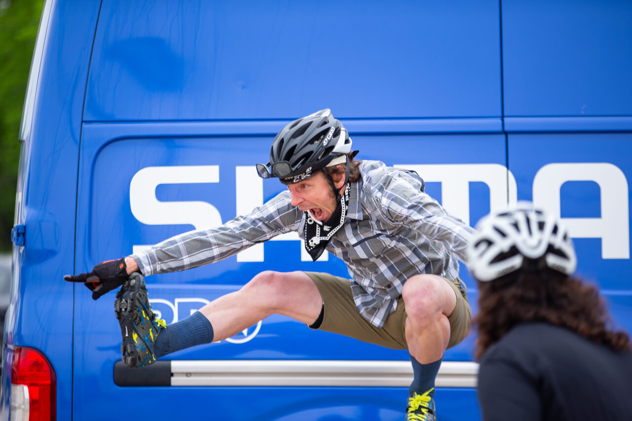 Past Shimano Gravel Alliance member jumping in excitement next the the big blue Shimano Van 
