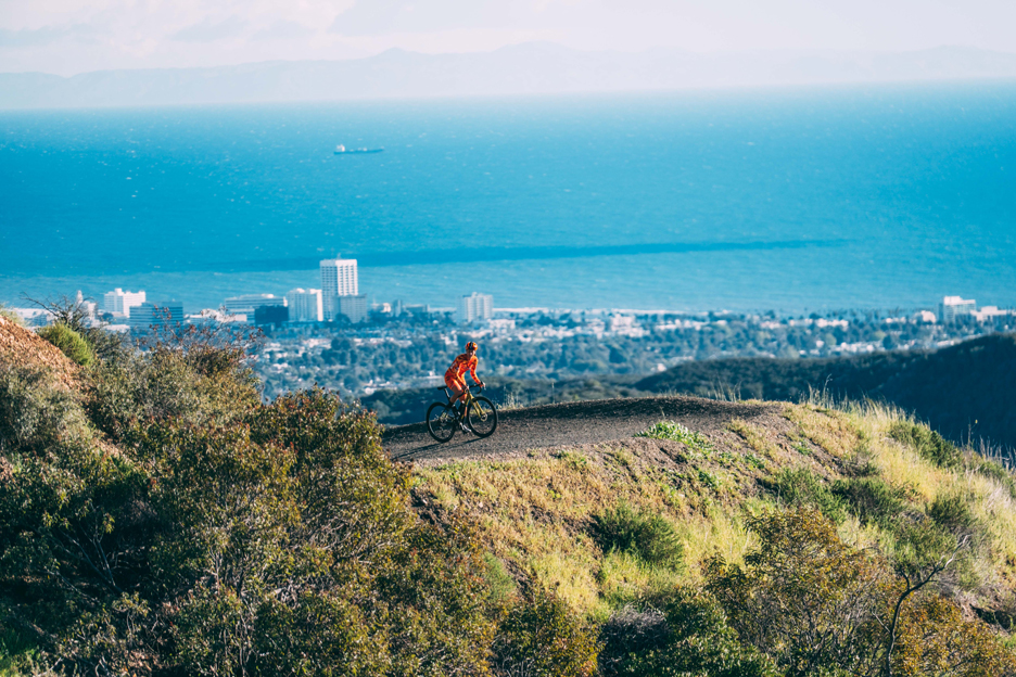 Izy King riding up hill in the LA mountains with the ocean in the background 